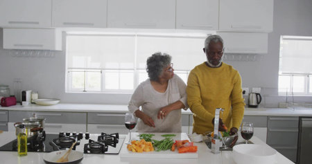 Preparing senior couple rinsing vegetables under faucet at kitchen counter, with wine glasses. Cooking, domestic, contemporary, lifestyle, wholesome, culinary, kitchenwareの写真素材