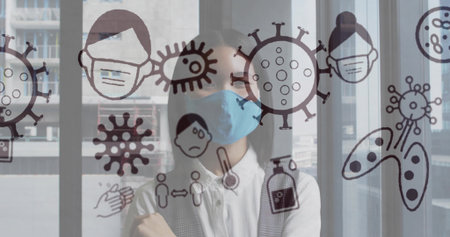 Standing Asian woman wearing blue mask behind glass partition, crossing arms with virus icons....