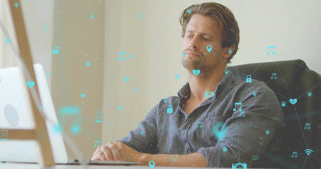 Leaning back man wearing denim shirt, working on white laptop at minimal desk with floating icons. Professional, digital connectivity, modern, technology, workspace, casual, innovationの写真素材