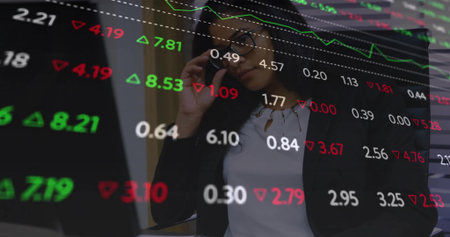 Businesswoman in suit analyzing market data on laptop and phone in office, with digital charts....