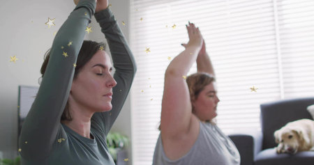 Practicing yoga two adult women raising arms overhead in living room, with resting dog on sofa. Mindfulness, relaxation, wellness, interior, calm, serenity, inspirationの写真素材