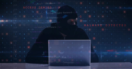 Typing hacker in balaclava and hoodie on laptop at desk in dark room, code, error messages....