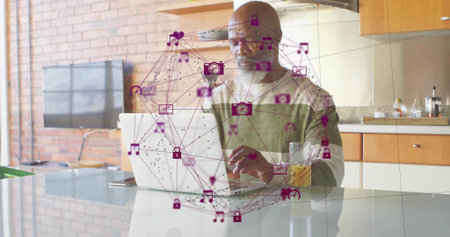 Working senior African American man typing on laptop at modern kitchen island, showing purple icons. Technology, connectivity, modern, lifestyle, innovation, homeoffice, relaxationの写真素材