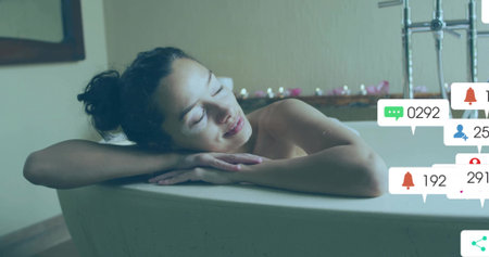 Leaning multiethnic woman on white bathtub rim in bathroom, candles, copy space. Relaxation, wellness, spa, serene, ambient, comfortの写真素材