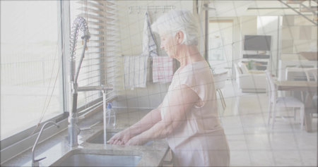 Washing senior woman cleaning hands under pull-down faucet at home kitchen, with granite countertop. Residential, modern, minimalistic, lifestyle, cozy, comfort, domesticの写真素材