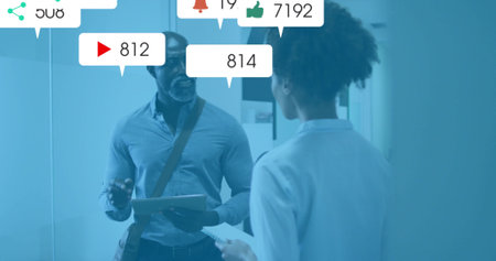 Discussing colleagues in suits sharing tablet at office corridor with floating social icons....