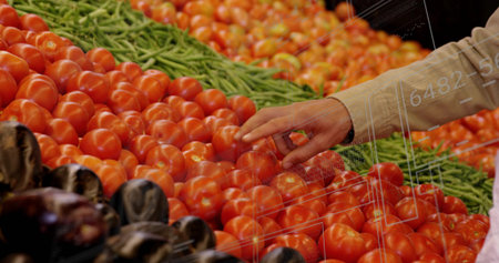 Touching tomato with shopper's hand in produce section, with red tomatoes green beans and eggplants....