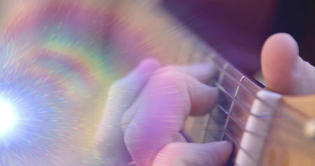 Pressing musician's left hand forming chord on acoustic guitar strings in studio with rainbow flare. Instrument, performance, artistry, color, lighting, creative, musicalの写真素材