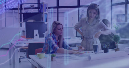 Women wearing plaid shirt, belted dress collaborating in open-plan office, reviewing color swatches....