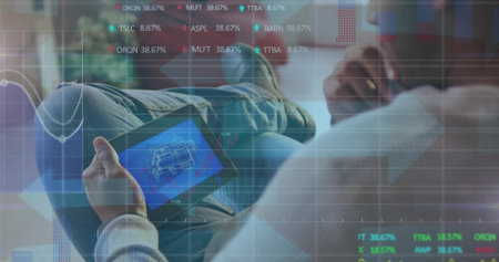 Reclining Asian man examining 3D building blueprint on tablet at home office, with ticker overlay. Innovation, technology, finance, remote, modern, workspace, analysisの写真素材