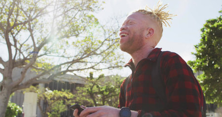 Smiling male student holding smartphone on campus path with backpack and wristwatch, copy space. Youth, outdoor, casual, nature, exploration, lifestyle, modernの写真素材