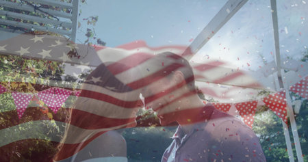 Couple in formal wear kissing under pergola in garden, with pennant banners, confetti, flag overlay. Romance, celebration, outdoor, festive, happiness, love, joyfulの写真素材