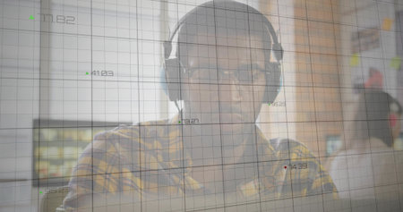 Developer interpreting grid with numeric readouts on laptop at office, with headphones glasses. Technology, data analysis, collaboration, modern workspace, digital, professional, innovationの写真素材