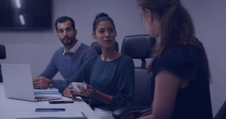 Holding mug, woman wearing teal blouse leading discussion in meeting room, with laptop and phones. Professional, collaboration, teamwork, corporate, brainstorming, modern, officeの写真素材