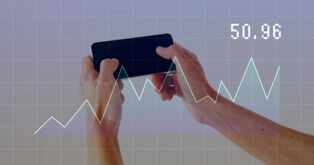 Hands grasping black smartphone horizontally in studio, with grid overlay, line graph reading 50.96. Technology, innovation, digital, analytics, data visualization, business, futurismの写真素材