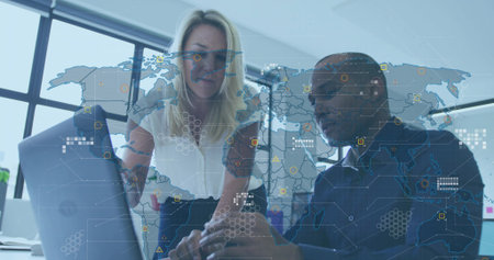 Collaborating duo in white blouse, dark shirt typing on laptop at office desk, with map overlay....