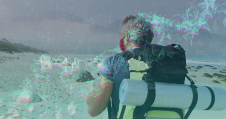 Adjusting backpack straps, mature hiker wearing face covering on rocky coastal beach, with foam mat. Adventure, outdoor, exploration, rugged, serenity, resilience, natureの写真素材