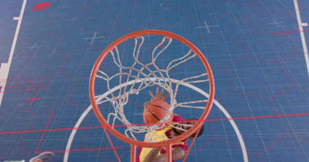 Player wearing yellow red uniform dunking orange basketball in blue court, featuring hoop with net....