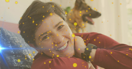 Reclining woman wearing shirt and smartwatch smiling on home sofa with German Shepherd golden bokeh. Relaxation, companionship, cozy, elegance, domestic, comfort, lifestyleの写真素材