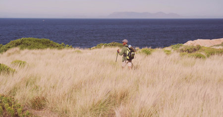 Walking hiker using trekking poles with backpack and sleeping pad on coastal dune, copy space....