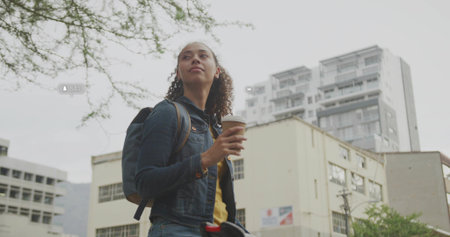 Standing woman holding coffee cup on city sidewalk, wearing denim jacket and backpack, copy space....