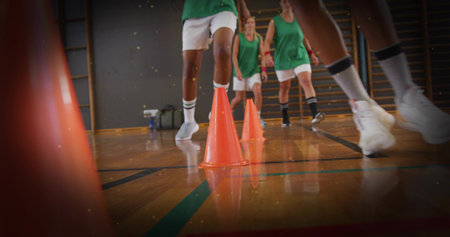 Leading athlete navigating bright orange cones in gym, wearing green jerseys, white shorts....