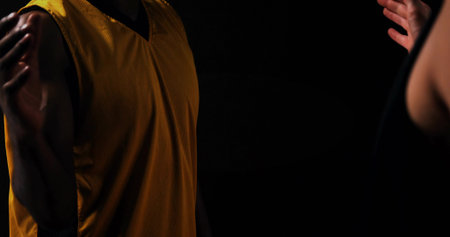 Facing basketball player wearing yellow mesh jersey in gym, with opponent in dark basketball jersey. Athletic, competition, sport, intensity, dynamic, team, focusの写真素材