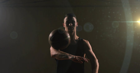 Balancing male athlete in jersey spinning basketball on finger inside dim gym, with lens flares. Athleticism, strength, focus, performance, determination, minimalist, dynamicの写真素材