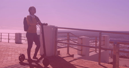 Leaning woman wearing activewear on promenade by guardrail, with scooter and backpack, copy space. Casualwear, outdoor lifestyle, scenic vista, urban leisure, youthful energy, waterfront, travelの写真素材