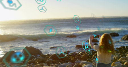 Capturing woman holding smartphone on beach at sunset, with hexagonal AR icons, copy space....