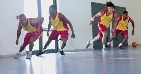 Performing defensive slide drill basketball players in yellow-red jerseys at gym, with basketball. Athletic, teamwork, focus, training, sport, fitness, motivationの写真素材