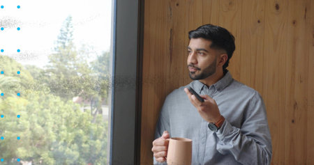 Talking Indian man holding mug, smartphone at work by glass window with wristwatch, copy space....