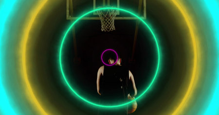 Standing basketball player in jersey holding basketball at center court under hoop, with neon rings....