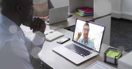Showing smiling coworker raising hand on laptop during online call at office desk with stationery....