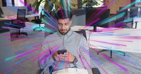 Holding smartphone, office worker sitting in mesh chair in modern office with desks monitors plants....