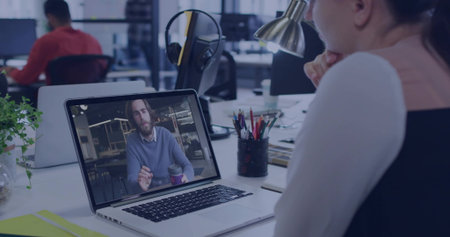 Laptop screen showing online call in open-plan office, with bearded colleague, coffee mug. Collaboration, teamwork, professional, productivity, digital, workspace, modernの写真素材