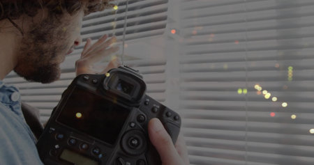 Holding DSLR camera, photographer wearing denim shirt peering through blinds in studio, copy space. Photography, professional, minimalist, interior, creative, artistic, contemplativeの写真素材