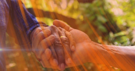 Holding senior couple clasped hands showing tender support in garden, with gold wedding ring. Companionship, affection, tenderness, longevity, serenity, outdoor, naturalの写真素材