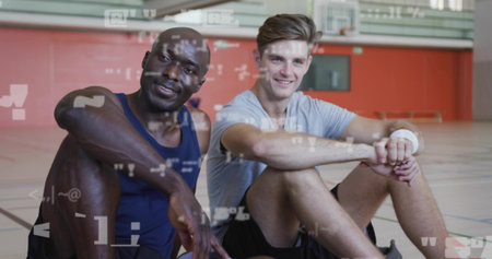 Resting athletes sitting on polished court with painted lines under overhead lights, bleachers back. Sportsmanship, camaraderie, performance, fitness, teamwork, recreation, vitalityの写真素材