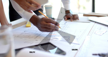 Marking blueprint with pencil, African American male wearing button-up shirt in office, with tablet....
