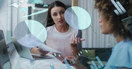 Analyzing data two businesswomen holding report and typing on laptop in office with glass partition. Professional, collaboration, modern, corporate, digital, analytics, teamworkの写真素材