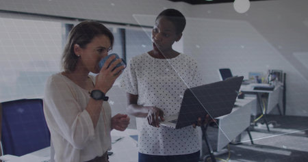 Two colleagues in business attire discussing laptop screen in modern office, with blue coffee mug....