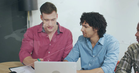 Pointing man in red shirt explaining on silver laptop at office table, with printed document. Collaboration, teamwork, modernoffice, professional, brainstorming, corporate, discussionの写真素材