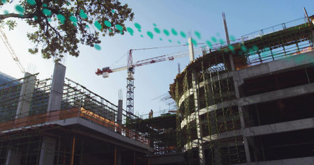 Construction worker wearing safety vest helmet surveying site, with tower crane and scaffolding....