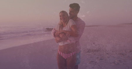 Embracing couple wearing swimwear gazing at horizon on sandy shoreline by sea at dusk, pink sky. Romance, serenity, leisure, vacation, silhouette, coastal, tranquilityの写真素材