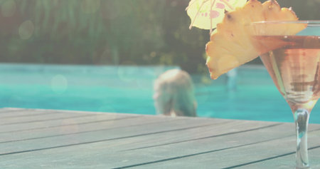 Resting cocktail glass with pineapple and paper umbrella on wooden deck by turquoise pool, copy space. Tropical, relaxation, leisure, outdoor, tranquil, vibrant, lifestyleの写真素材