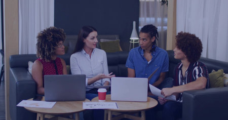 Discussing colleagues exchanging ideas in office lounge, with laptops, papers and red coffee cup....