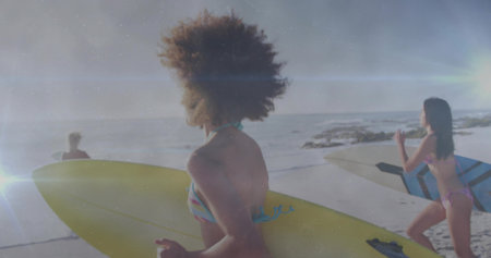 Walking three women wearing bikinis carrying surfboards along sandy beach at sunset, ocean waves. Summertime, friendship, adventure, lifestyle, athletic, coastal, vibrantの写真素材