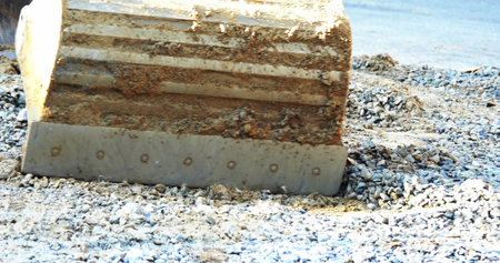 Pressing excavator bucket blade into loose gravel and pebbles on riverbank, with mud and bolt heads. Industrial, machinery, rugged, construction, outdoor, durability, textureの写真素材