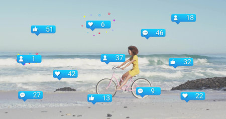 Riding woman in yellow dress on pink bicycle along wet beach, with floating social media icons....